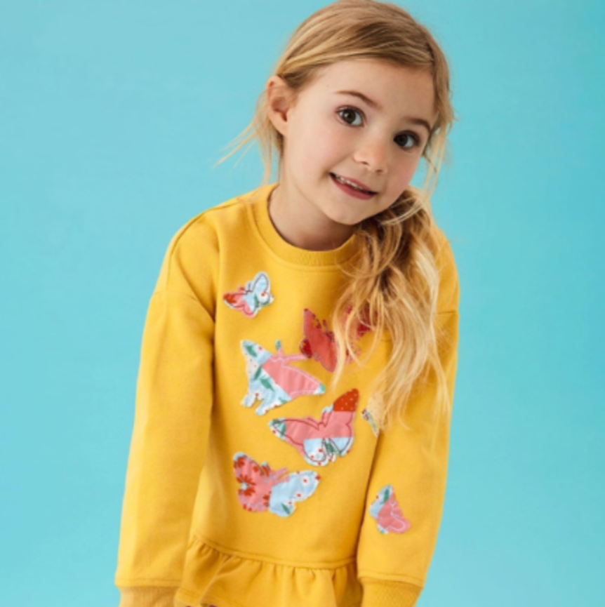 Young girl wearing a yellow sweater with colorful butterfly designs on a blue background